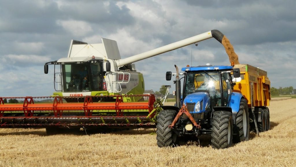 Servicios A modern combine harvester and tractor working together to harvest wheat in a sunny outdoor field.