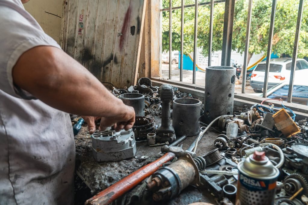 Inicio Mechanic organizing auto parts in a busy workshop, surrounded by tools and equipment.